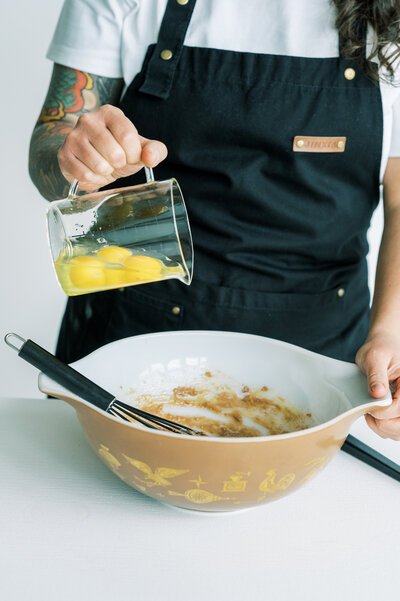 owner - Johannah pouring a measuring cup full of raw egg into a mixing bowl