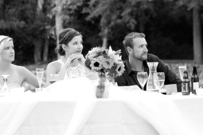 A bride and groom listen to speeches during their outdoor backyard reception.