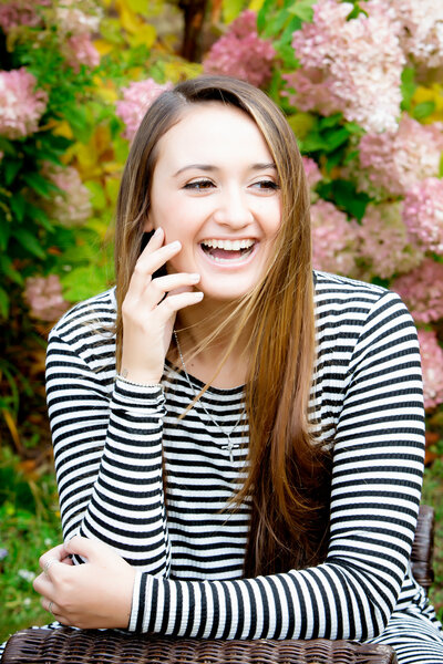 High school senior girl wearing a black & white striped dress with her hand on her face, laughing, posing for a South Shore MA Senior photographer