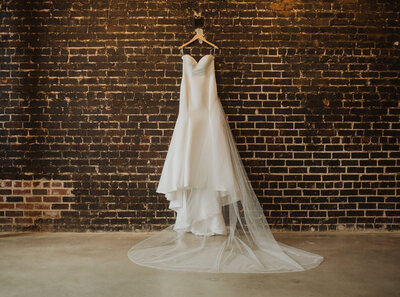 A wedding dress hanging on a hook on a brick wall