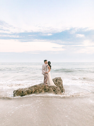 photo of bride and groom on rock in the ocean in los angeles beach