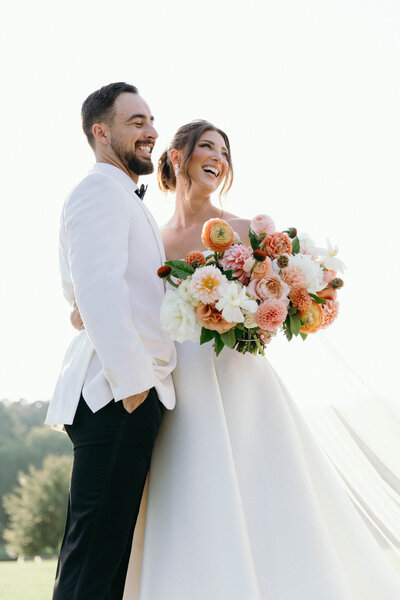 A delightful moment captured as the groom and bride, with a bouquet in hand, embrace each other, sharing smiles and happiness