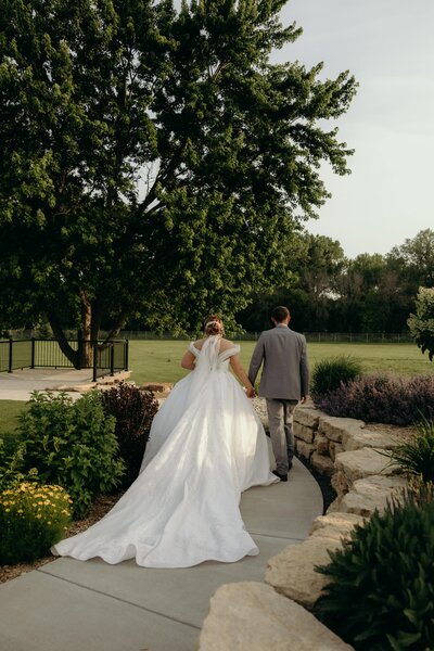 A bride's long train flows behind her as a couple walks hand in hand together.