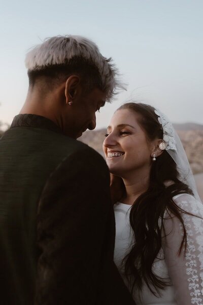 Bride smiling at her partner during an intimate moment outdoors, with soft evening light on her face.