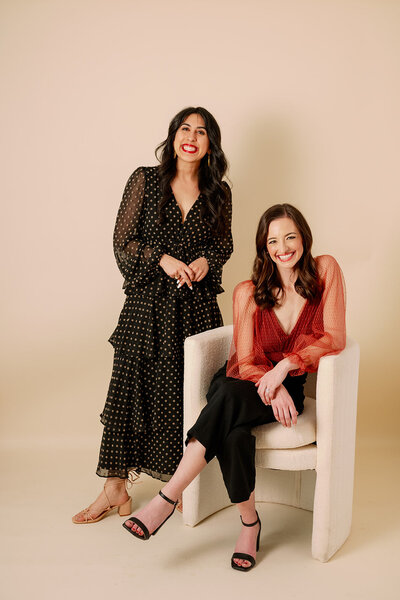 One woman stands beside another seated in a chair