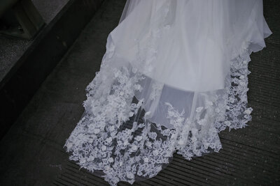 detail shot of lace wedding dress train flowing behind the bride as she walks