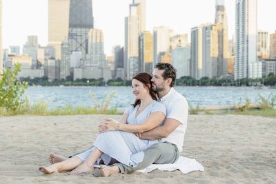 man and woman sitting on beach next to city