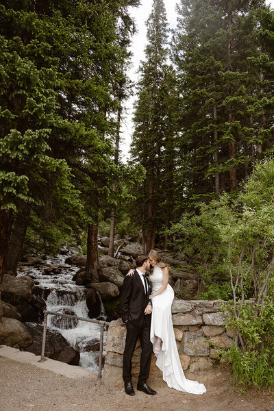 A photo of a bride holding on to her groom in front of a waterfall taken by Adventure elopement photographer in Idaho Springs Colorado. 