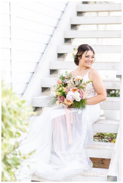 Bride sites on barn stairs holding bouquet of flowers at Homestead on McVey in Victor, MT