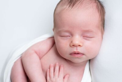 Minimalistische newborn fotoshoot aan huis met een lichte achtergrond. Leg de unieke details van je baby vast in een rustige en natuurlijke omgeving.