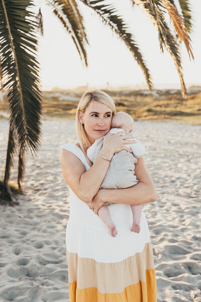 A mother holds her small baby on the beach in Coronado