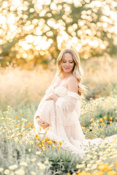 A maternity session by Bay area photographer shows a woman standing and caressing her bump in a flower field of poppies.