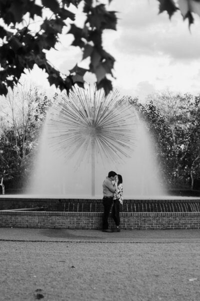 newly engaged couple sharing a romantic moment in front of the iconic Dandelion Fountain in Downtown Houston, captured in black and white during their portrait session.