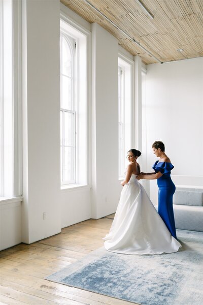 bride and her mother putting on her dress on her wedding day