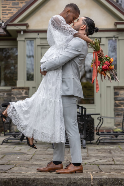 interracial, newly married couple share a passionatre moment captured by Scranton Weding Photographer Eric Boylan in front of Brasenhill Mansion in Annville, Pennsylvania. Bride is wearing a white baltic born dress and holding a yellow and red bouquet