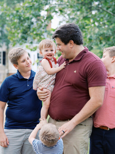 A dad holding a baby as the dad and siblings look at the baby by Katie Stansfield Photography, a Richmond family photographer.