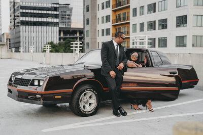 woman sitting in a black car with man leaning against car next to her
