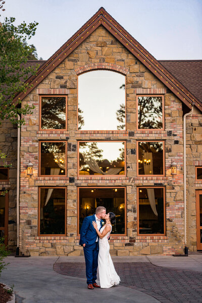 Groom in a blue suit and Bride in a white dress kissing in front a house