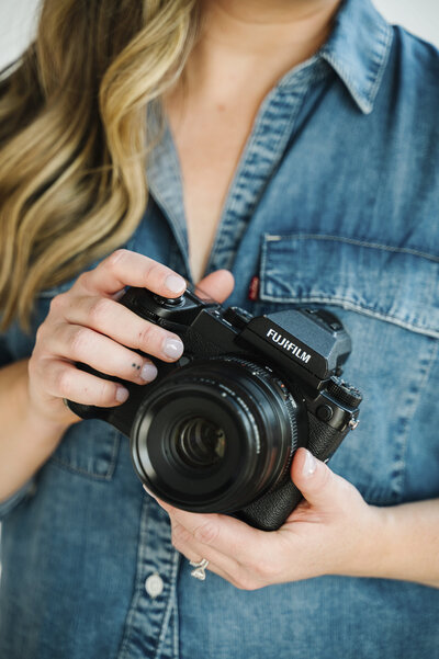 A close up photo of Krista Marie, a brand photographer for women, holding her camera in front of her blue denim shirt