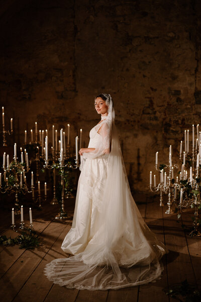 A person in a wedding dress looking over their shoulder surrounded by candles 