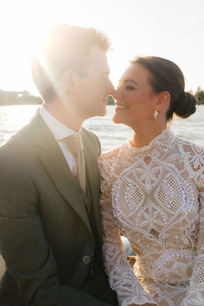 Bruidsshoot op het water tijdens golden hour, met een bruid en bruidegom die elkaar liefdevol aanraken in warm tegenlicht