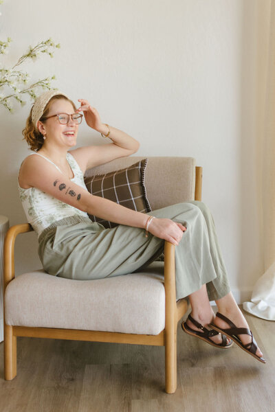 Lillian, a virtual assistant for wedding creatives, smiling while seated on a modern tan chair during a branding session.