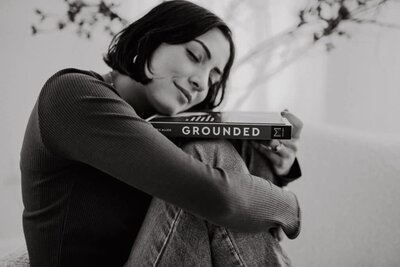 Minimalist black-and-white branding portrait of a woman peacefully hugging a book titled 'Grounded,' conveying calm and confidence.