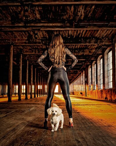 Woman wearing leather pants and Louboutin heels poses with hands on hips with white poodle at the McKinney Cotton Mill.