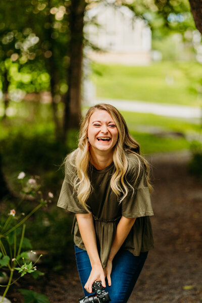 Staci smiling and crouched in a green wooded area, capturing fun and approachable energy