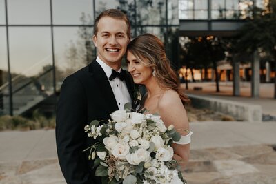 A Texas bride and groom smiling in front of a building at dusk, captured beautifully by a talented wedding videographer.