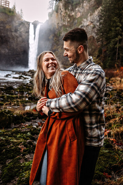 Experience the magic of the Pacific Northwest with this stunning photo of a couple embracing in front of a majestic waterfall. Perfect for those seeking adventure and romance in their photography.
