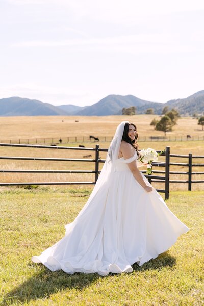 Bride twirling in her wedding dress in front of the fence line at Spruce Mountain Ranch — Colorado ranch wedding portrait