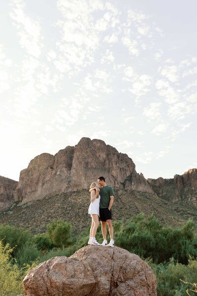 Couple stand and hug on top of a rock at Saguaro Lake
