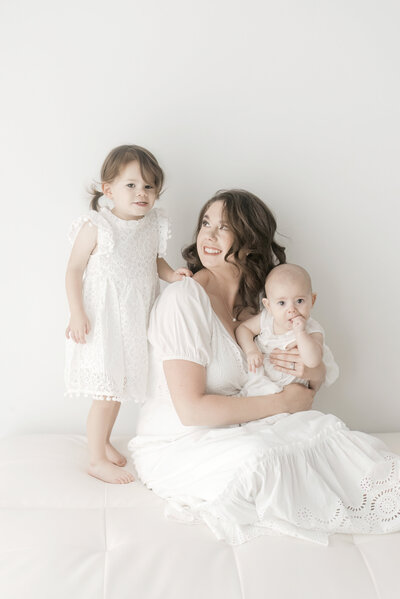 Mother, toddler, and baby in white dress with white background