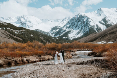 Couple walks hand-in-hand beside snowy peaks in Breckenridge captured by elopement photo and video team.