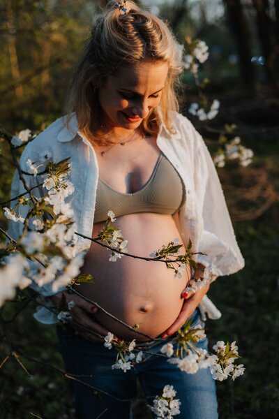 Fotoshooting zwischen Kirschenblüten, werdende Mutter hält ihren Babybauch