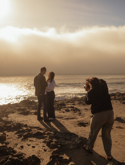 photographer capturing candid engagement photos of couple at the Oregon coast during sunset