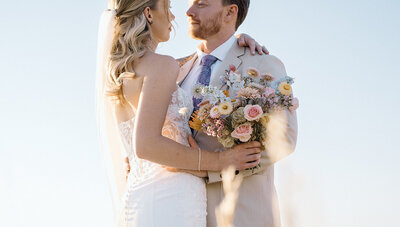 bride and groom caress in the bright sun after wedding ceremony in Colorado