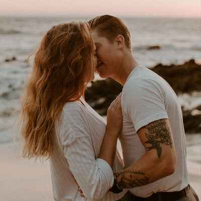The couple shares an intimate kiss at the base of the California cliffs on the beach. The sunset was the perfect shade of pink and orange for their anniversary photos.
