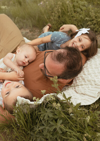 Playful dad snuggling his three children on a blanket at.