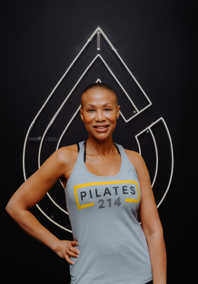 Headshot of Pilates instructors Amber standing in front of Pilates214 neon logo sign.