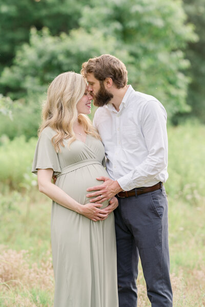 A pregnant couple kisses while standing in tall grass in Moorestown.