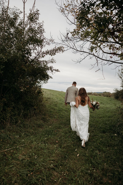 bride and groom walking through grass together