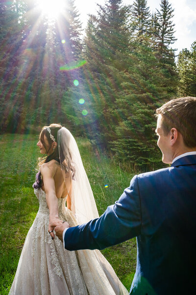 Bride and groom standing in a pine forest with warm sunflare shining through the trees at Mountain View Ranch in Colorado.