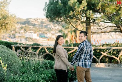 Engaged couple look back at the photographer while holding hands in Heisler Park in Laguna Beach