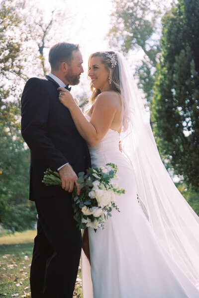 Bride and groom embracing in natural light with a lush outdoor backdrop.