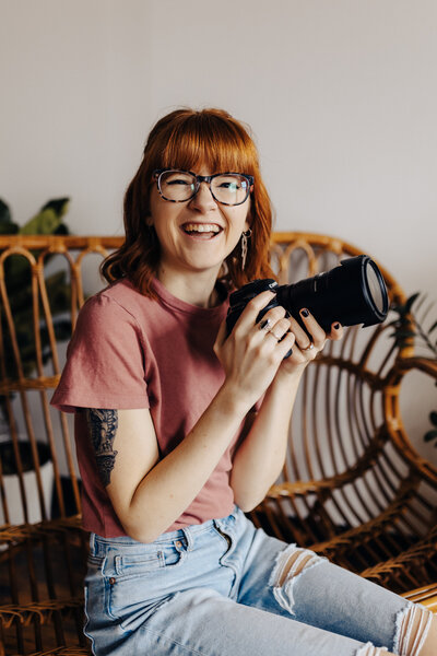woman sitting down smiling while holding a large camera