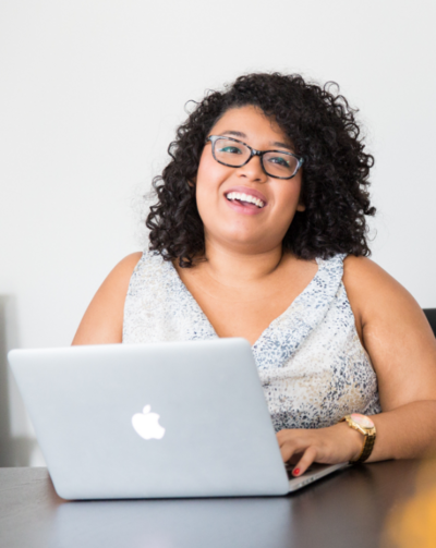 Caramel-skinned woman smiles while working on laptop