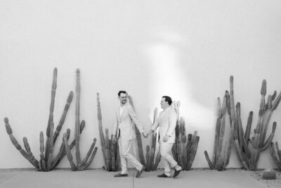 Grooms holding hands by modern desert cacti walls at Andaz Scottsdale Wedding Venue, a stylish moment highlighting Andaz Scottsdale Wedding Photographers.