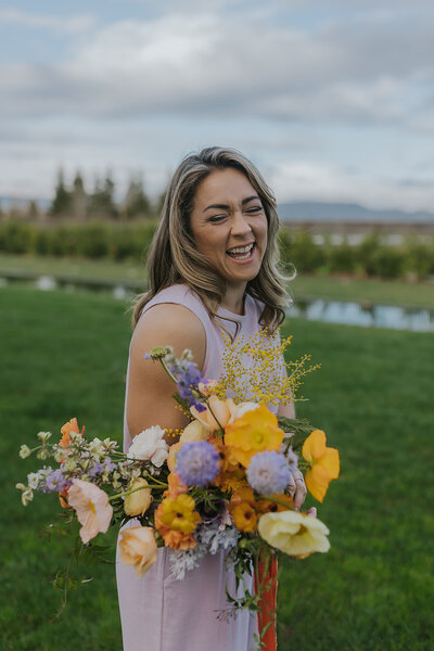 Alexandra laughing outside holding a purple and yellow spring inspired bouquet